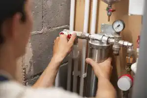 Professional plumber fixing residential plumbing pipes and adjusting a valve on a home water filtration system.