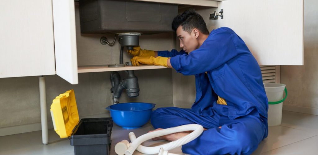 asian-plumber-blue-overalls-clearing-blockage-drain